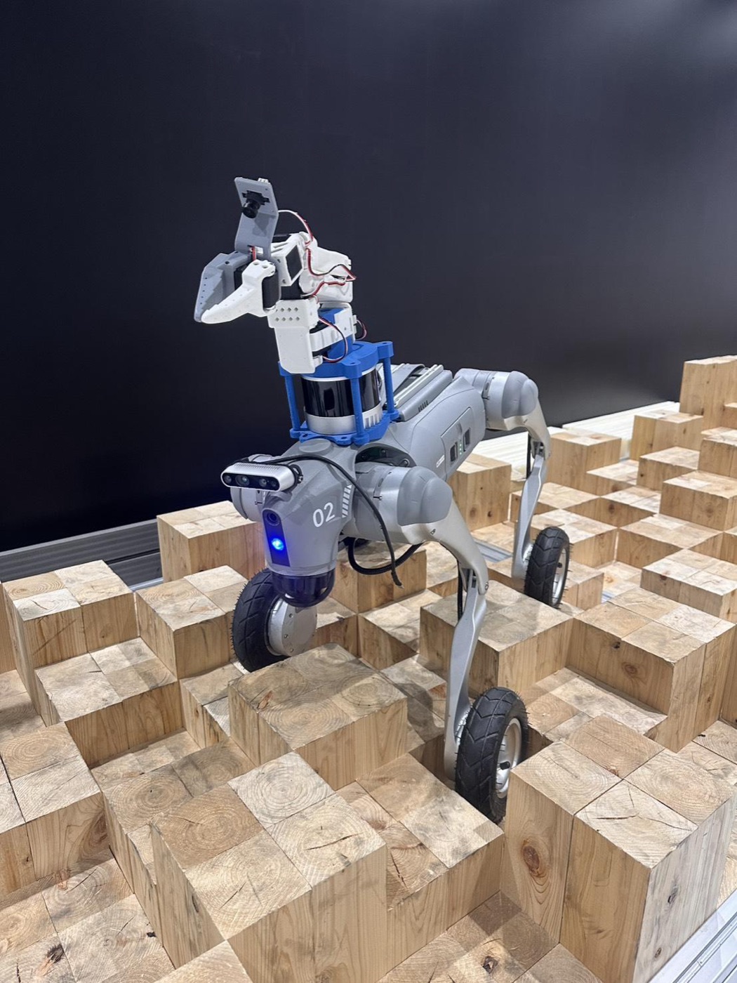 アーム・LiDAR・カメラを載せた Go2W が木のブロックの上に立つ